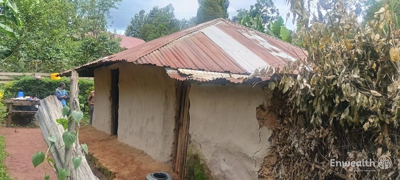 A small house with mud walls and a rusted, patched iron roof.